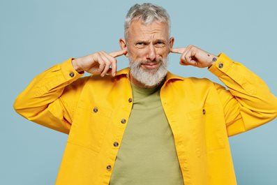 Elderly man in yellow shirt cover ears with hands fingers do not want to listen scream