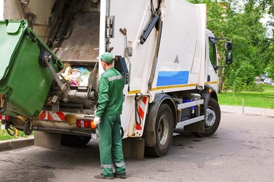 worker operating garbage compressor track in residential area